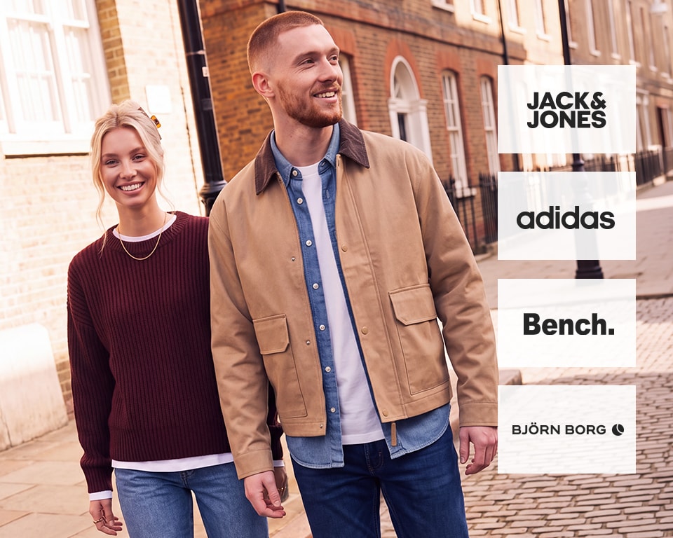 Lachend stel. Vrouw in een bordeauxrode ribbel gebreide trui en lichte jeans; man in een beige jas en spijkerhemd.